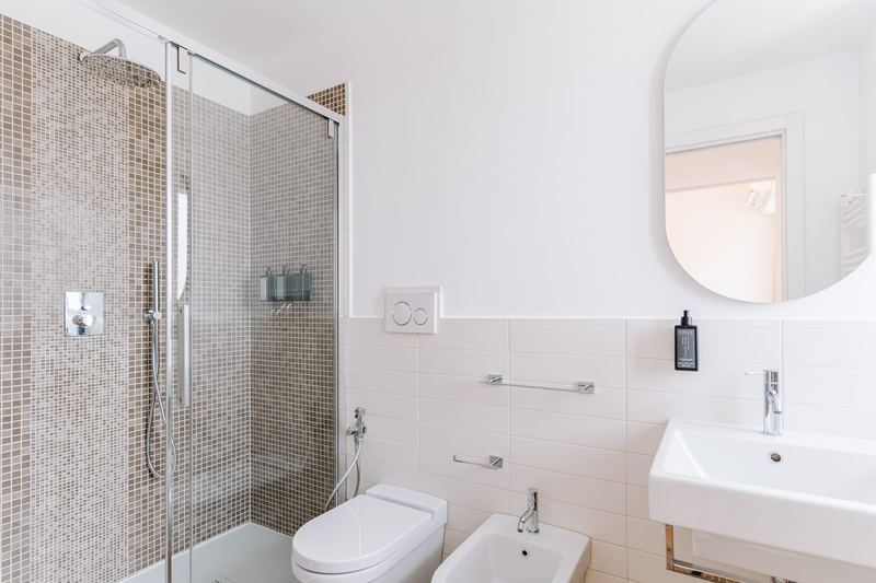 Bagno con doccia rivestita in mosaico e sanitari sospesi