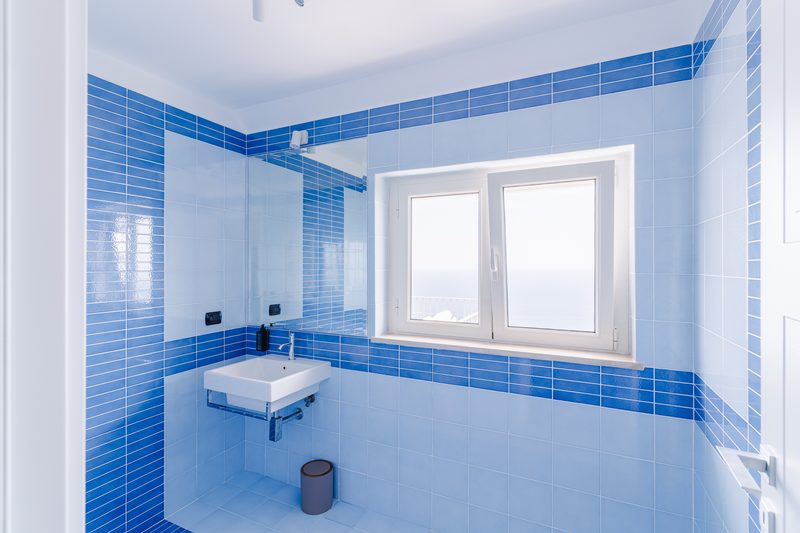 Bagno rivestito in maioliche blu con finestra vista mare
