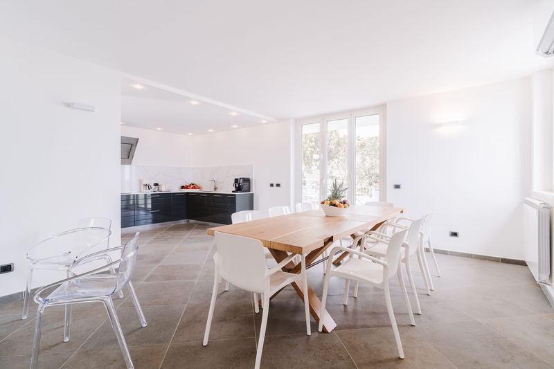 Sala da pranzo interna con grande tavolo in legno e cucina open space