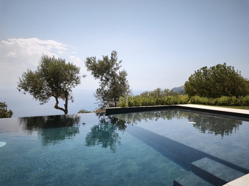 Piscina a sfioro tra gli ulivi con riflessi sul mare